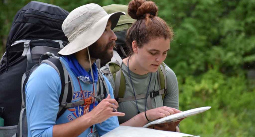 Two people wearing backpacks examine something in their hands